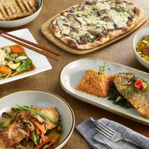 A table spread of healthy dishes, including fish, pizza, and stir-fry, from A Votre Santé.