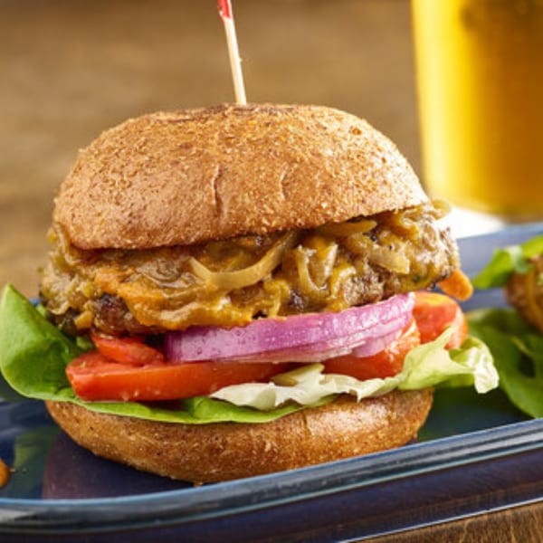 A healthy burger with caramelized onions, lettuce, tomato, and red onion on a whole wheat bun.