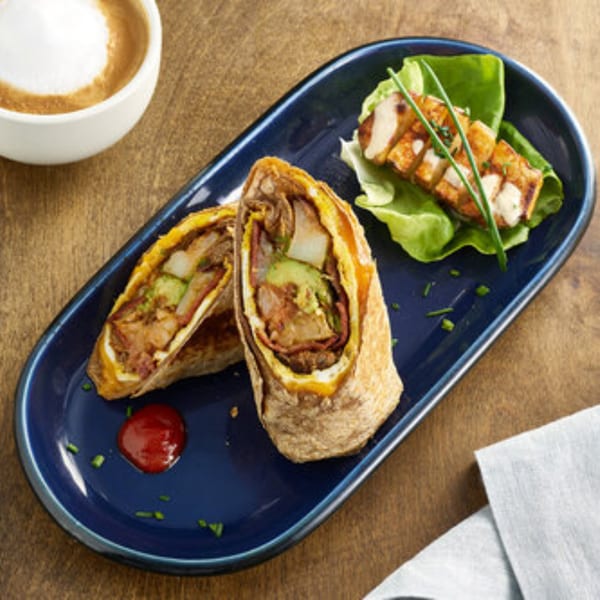 A Votre Santé breakfast burrito, chicken, and a latte on a dark blue plate and wooden table.