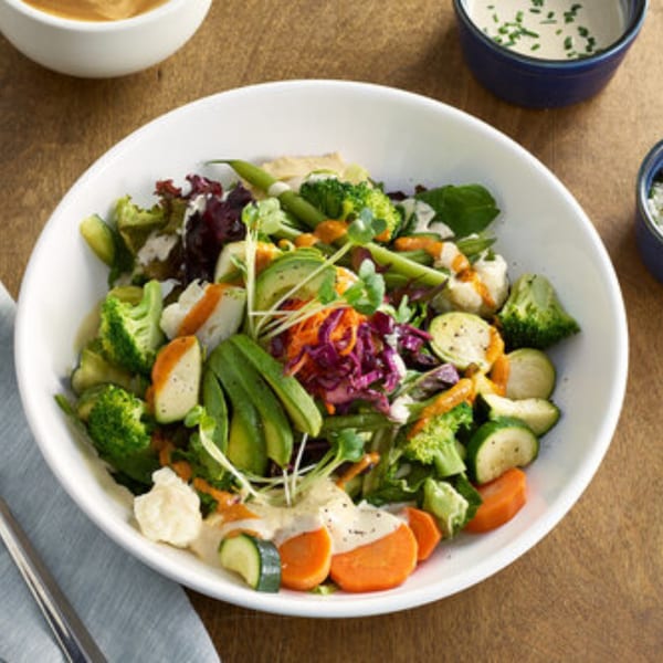 A Votre Santé's healthy salad with broccoli, avocado, carrots, and mixed greens in a white bowl.