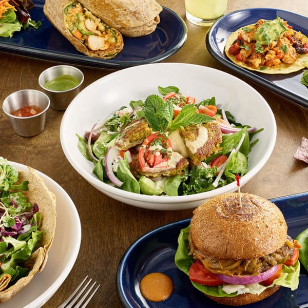 A table spread with various healthy dishes including a falafel salad, burger, wrap, and taco.