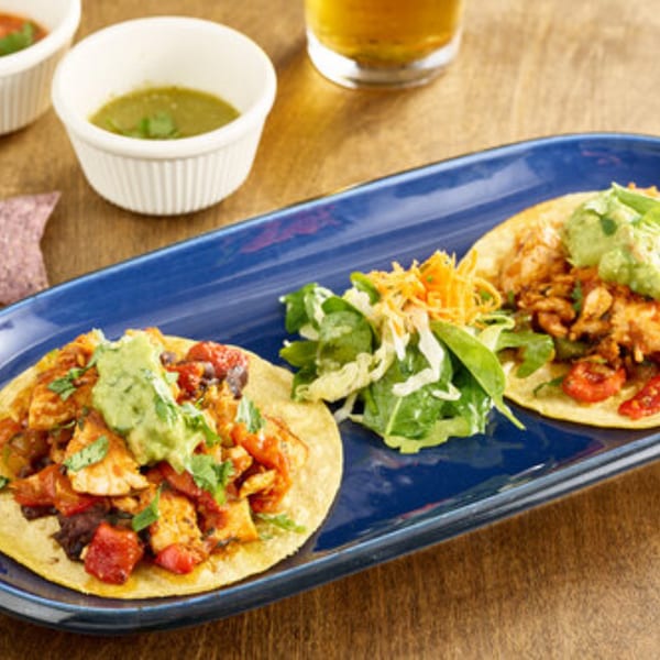 Two healthy tacos with chicken, tomatoes, and guacamole, served with a side salad and salsa.