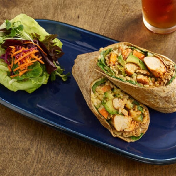 Two healthy chicken and avocado wraps with a side salad on a blue plate.