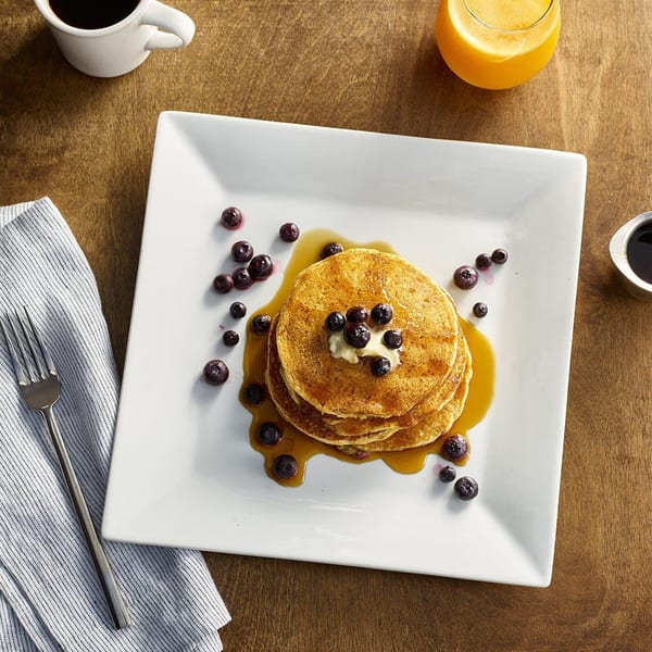 Stack of blueberry pancakes with butter and syrup, coffee, and orange juice on a wooden table.