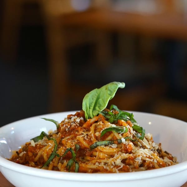A Votre Santé's healthy spaghetti with tomato sauce, parmesan, and fresh basil in a white bowl.