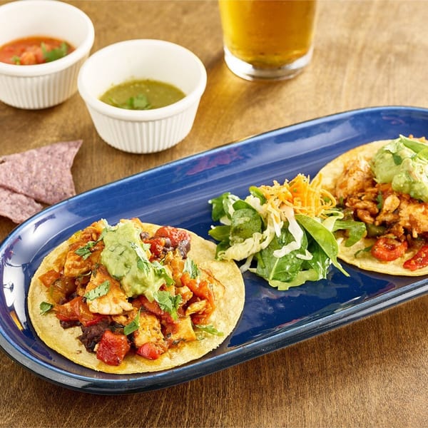 Two healthy fish tacos with guacamole, salsa, and a side salad on a blue plate.
