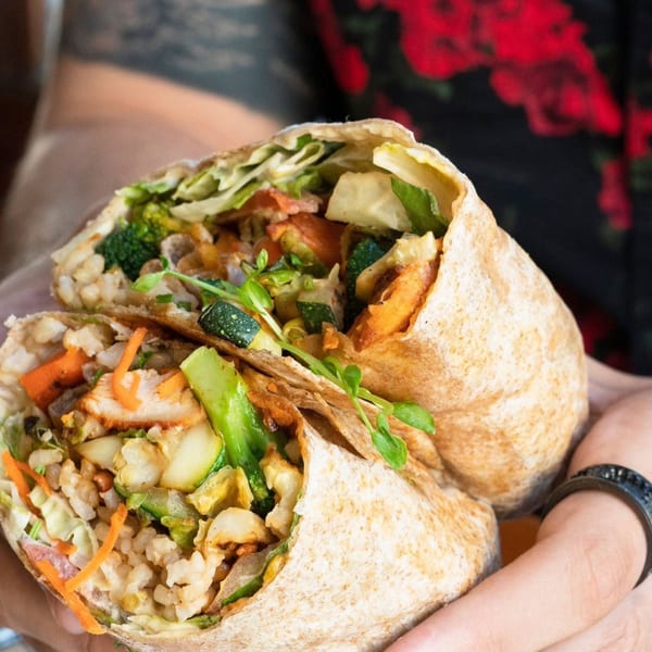 Hands holding a healthy A Votre Santé burrito, cut in half, filled with chicken, rice, and vegetables.