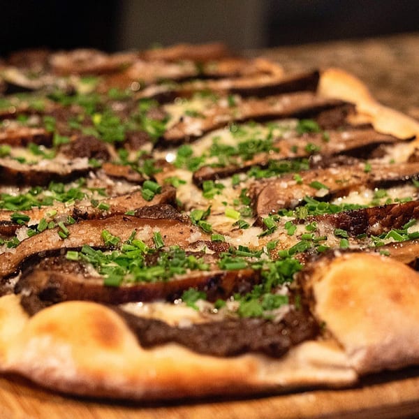 Close-up of a healthy flatbread pizza topped with mushrooms, cheese, and fresh chives.