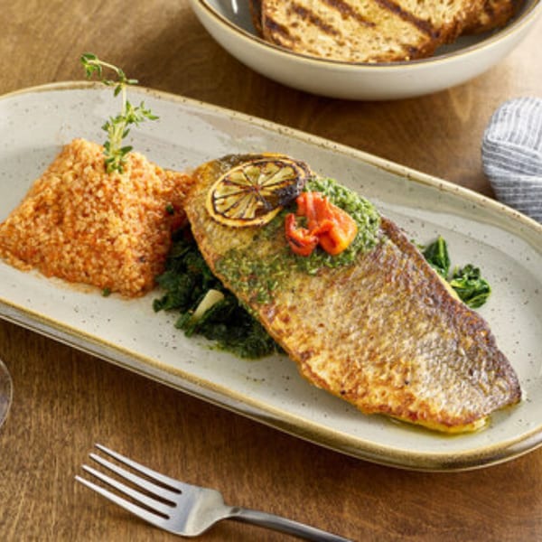 A Votre Santé's grilled fish with couscous, greens, lemon, and red peppers on a rectangular plate.