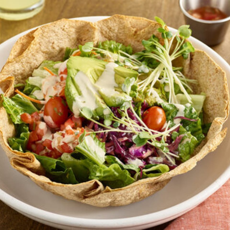 A Votre Santé's healthy taco salad in a crispy tortilla bowl, topped with avocado and dressing.